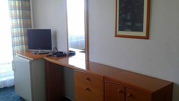 A hotel room with a wooden desk, a small refrigerator, a mirror, and a framed picture on the wall.