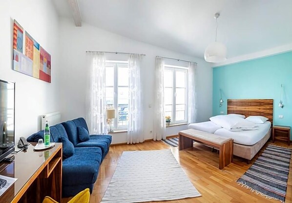 A modern hotel room with a bed, a sofa, a desk, and a large window. - Altstadthotel Wetzel (Mühldorf am Inn)