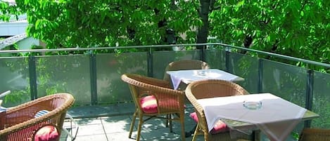 An outdoor patio with wicker furniture and a table, surrounded by greenery.
