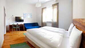 Habitación de hotel con cama, un escritorio y una silla, televisión y ventana con cortinas.