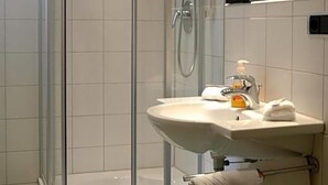 Un baño con ducha envuelta en vidrio, un lavamanos con espejo y un perchero con toallas.