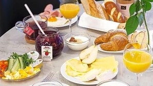 Una mesa de desayuno con diversas opciones de comida, incluyendo cruasanes, fruta y una botella de vino.