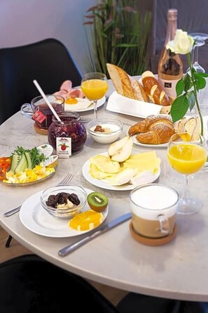 Mesa de café da manhã com diversos alimentos, incluindo croissants, frutas e uma garrafa de vinho.