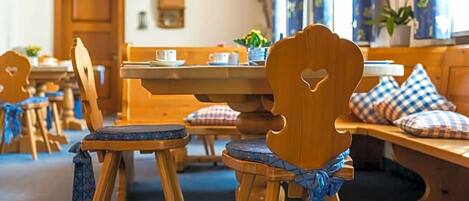 A cozy dining area with wooden furniture, including chairs and a bench, and a table with a cup and saucer.