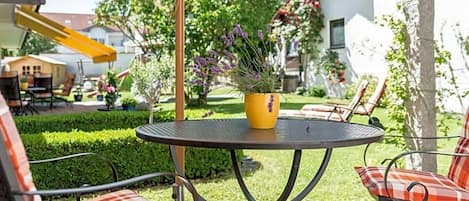 An outdoor patio with a round table and chairs, a yellow planter with flowers, and a yellow slide in the background.