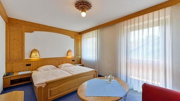Ein Hotelzimmer mit einem hölzernen Bett, Nachttischlampen, einem Tisch mit blauer Tischdecke und einem roten Sessel.