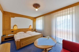 Una habitación de hotel con una cama de madera, lámparas de noche, una mesa con mantel azul y una silla roja.