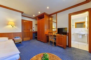 Una habitación de hotel con cama, escritorio, silla, televisor y baño.