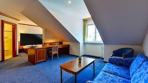 Ein Zimmer mit schrägem Dach, einer Couch, einem Couchtisch, einem Fernseher und einem Schreibtisch mit Stuhl.