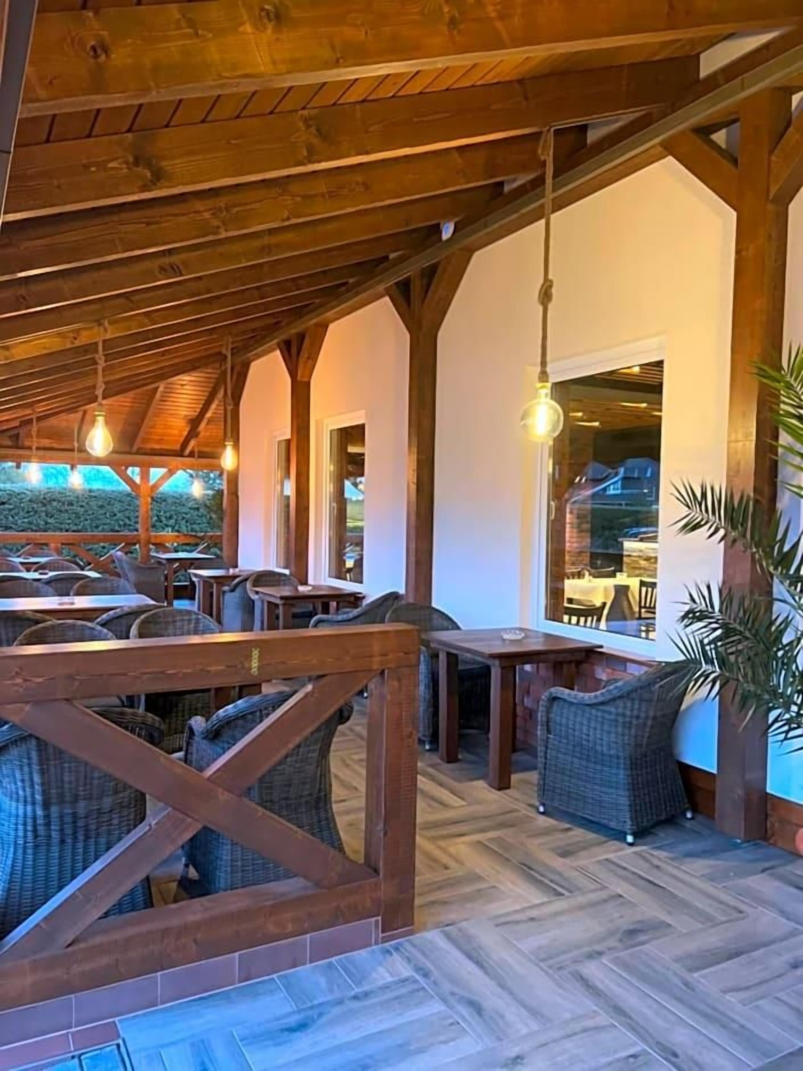An outdoor seating area with wooden beams, wicker furniture, and hanging light fixtures.