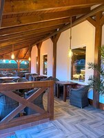 Un espacio al aire libre con vigas de madera, mobiliario de mimbre y lámparas colgantes.