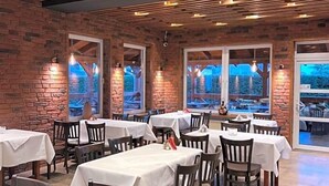 Restaurante com paredes de tijolo, vigas de madeira no teto e mesas preparadas para refeições.