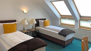Quarto de hotel com duas camas, claraboia, mesa de cabeceira com luminárias e vista para o exterior.