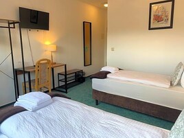 Habitación de hotel con dos camas, un escritorio, una silla, un televisor y obras de arte en la pared.