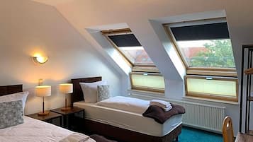 Ein Hotelzimmer mit zwei Betten, einem Fenster, einem Heizkörper und einem Nachttisch mit Lampen.