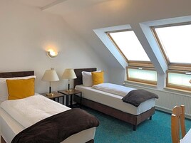 Habitación de hotel con dos camas, tragaluz, mesita de noche con lámparas y vistas al exterior.