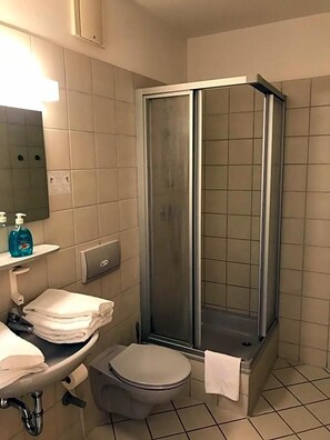 Un baño con inodoro, lavamanos y cabina de ducha con mampara de vidrio.