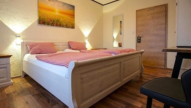 A bedroom with a bed, bedside tables, a wooden dresser, a chair, and a door. - Landhotel Restaurant Beckmann (Heiden)
