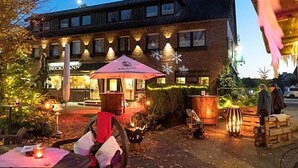A building with a brick facade, outdoor seating area with tables and chairs, and a red umbrella. - Landhotel Restaurant Beckmann (Heiden)