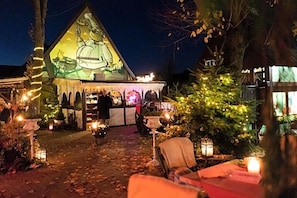 Un edificio con techo triangular y un mural, rodeado de mesas al aire libre e iluminado por velas.