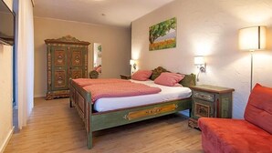 A bedroom with a wooden bed, a red sofa, a wooden cabinet, and a painting on the wall. - Landhotel Restaurant Beckmann (Heiden)