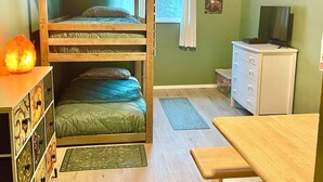 Une chambre avec un lit superposé, un bureau, une commode, un téléviseur et une fenêtre avec des rideaux.