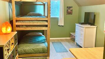 A room with a bunk bed, a desk, a dresser, a television, and a window with curtains.