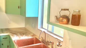 A kitchen with green cabinets, a copper sink, and a window above the counter.