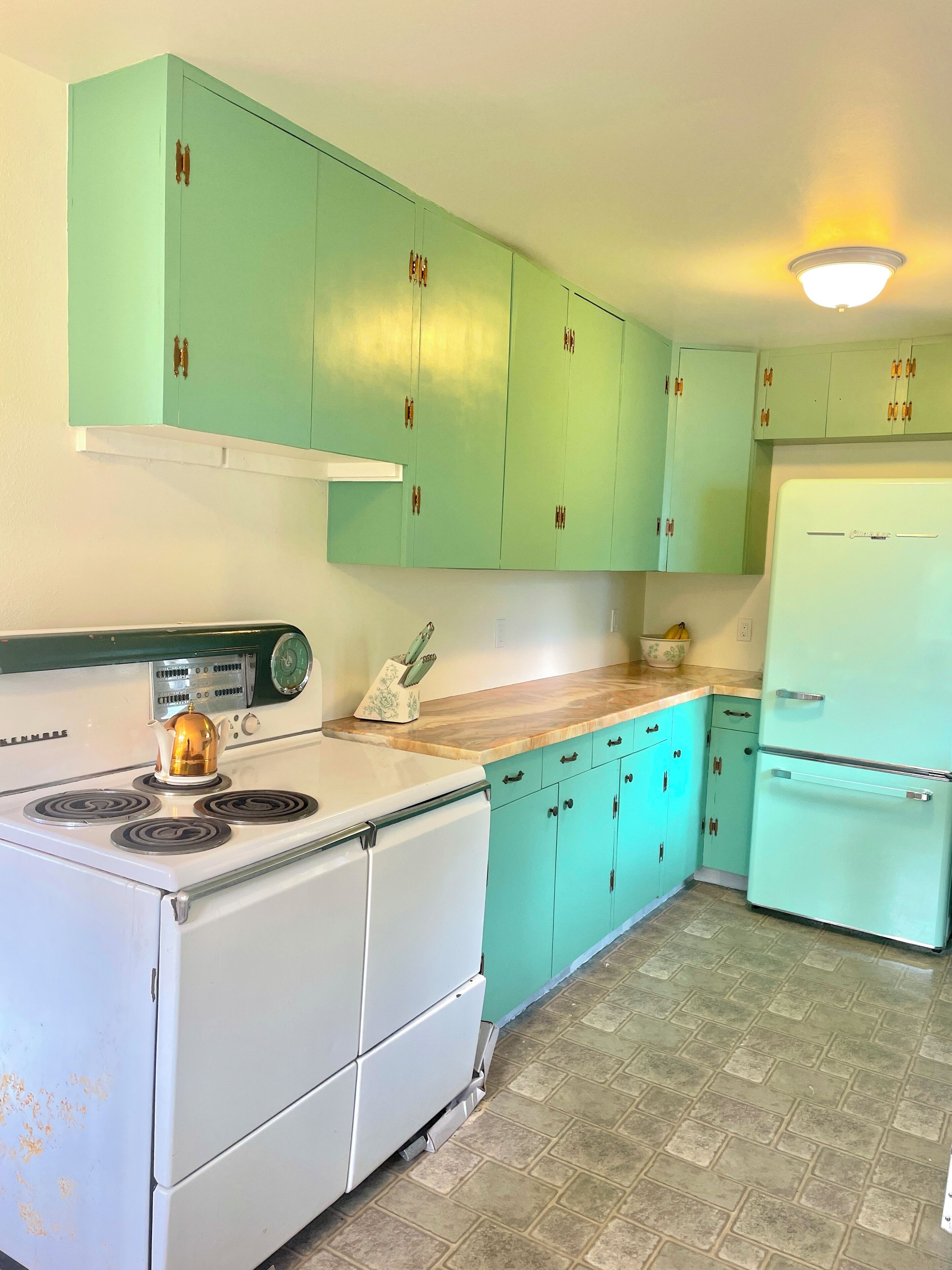Una cocina con armarios color turquesa, una estufa blanca y un refrigerador blanco.