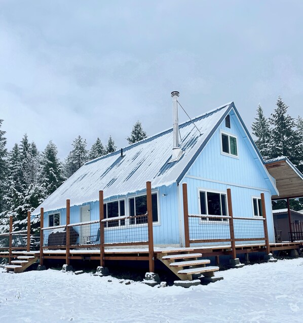 Une cabane bleue avec un toit en métal, une terrasse en bois et une cheminée.