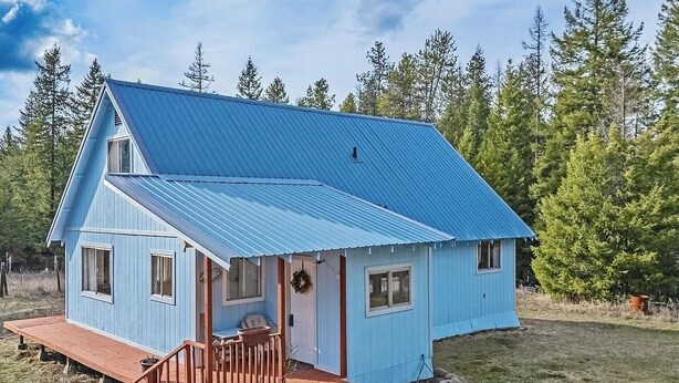 Une maison de plain-pied à l’extérieur bleu et au toit métallique, entourée d’une pelouse et d’arbres.
