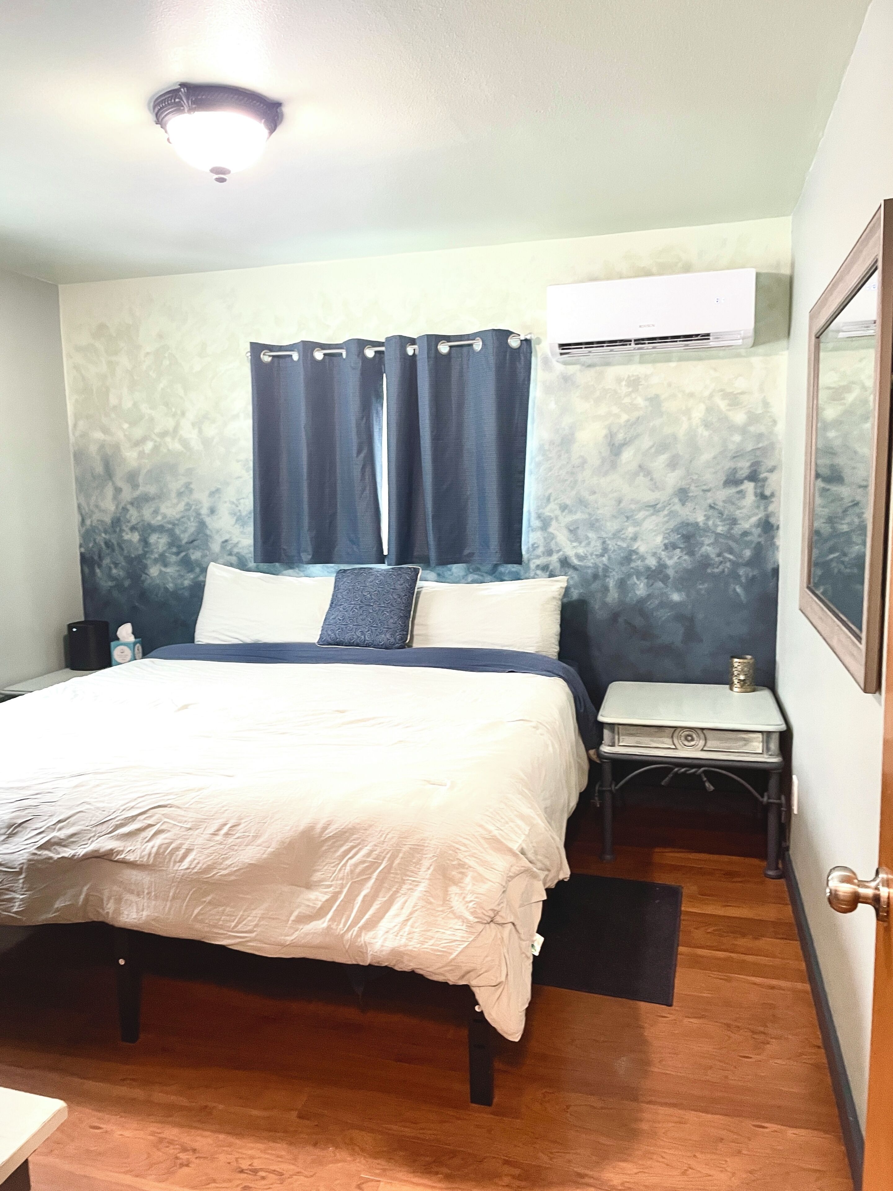 Un dormitorio con cama, mesita de noche, equipo de aire acondicionado y una puerta.
