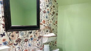 Une salle de bain avec un papier peint à motifs floraux, un lavabo blanc, un miroir et des toilettes.