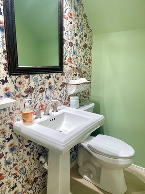 Un baño con papel tapiz floral, un lavamanos blanco, un espejo y un inodoro.