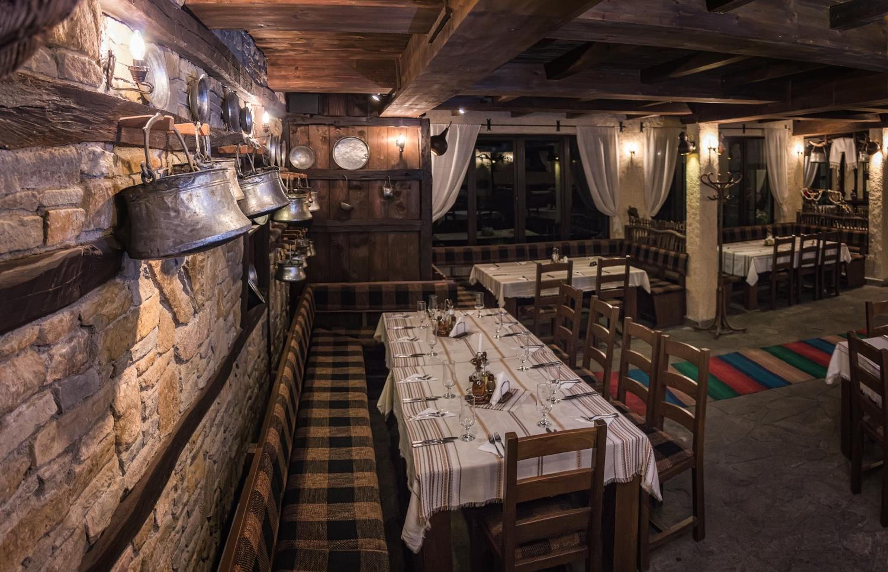 A rustic dining area with wooden walls, a long table set for a meal, and a stone floor.
