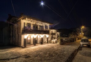 A two-story building with a balcony, stone flooring, and string lights. - Family Hotel Strannopriemnitza (Troyan)