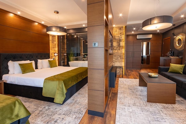 A modern hotel room with a large bed, a sitting area with a coffee table, and a separate living area with a sofa and a TV. - Family Hotel Strannopriemnitza (Troyan)