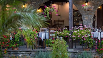 An outdoor dining area with stone arches, hanging flower baskets, and tables set for dining.
