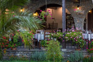 An outdoor dining area with stone arches, hanging flower baskets, and tables set for dining. - Family Hotel Strannopriemnitza (Troyan)