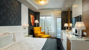 Hotellihuone, jossa on sänky, keltainen nojatuoli, työpöytä lampun kanssa ja televisio.