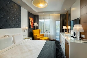 A hotel room with a bed, a yellow armchair, a desk with a lamp, and a TV. - Family Hotel Strannopriemnitza (Troyan)