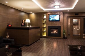 A hotel lobby with a reception desk, a flat-screen TV, a fireplace, and a modern ceiling design. - Family Hotel Strannopriemnitza (Troyan)
