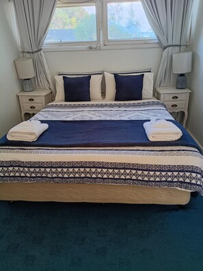 A bed with a patterned bedspread, two pillows, and two folded towels. - Wimmera Motel (Nhill)