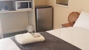 A hotel room with a bed, a desk with a computer and a microwave, a refrigerator, and a mirror.