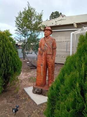 A statue of a man in a hat and work clothes, standing on a concrete base surrounded by greenery. - Wimmera Motel (Nhill)