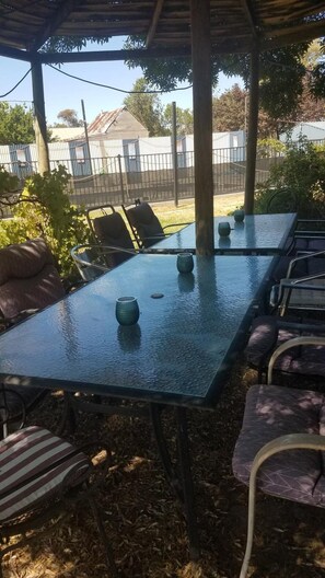 An outdoor covered dining area with a table and chairs, surrounded by foliage and a fence. - Wimmera Motel (Nhill)