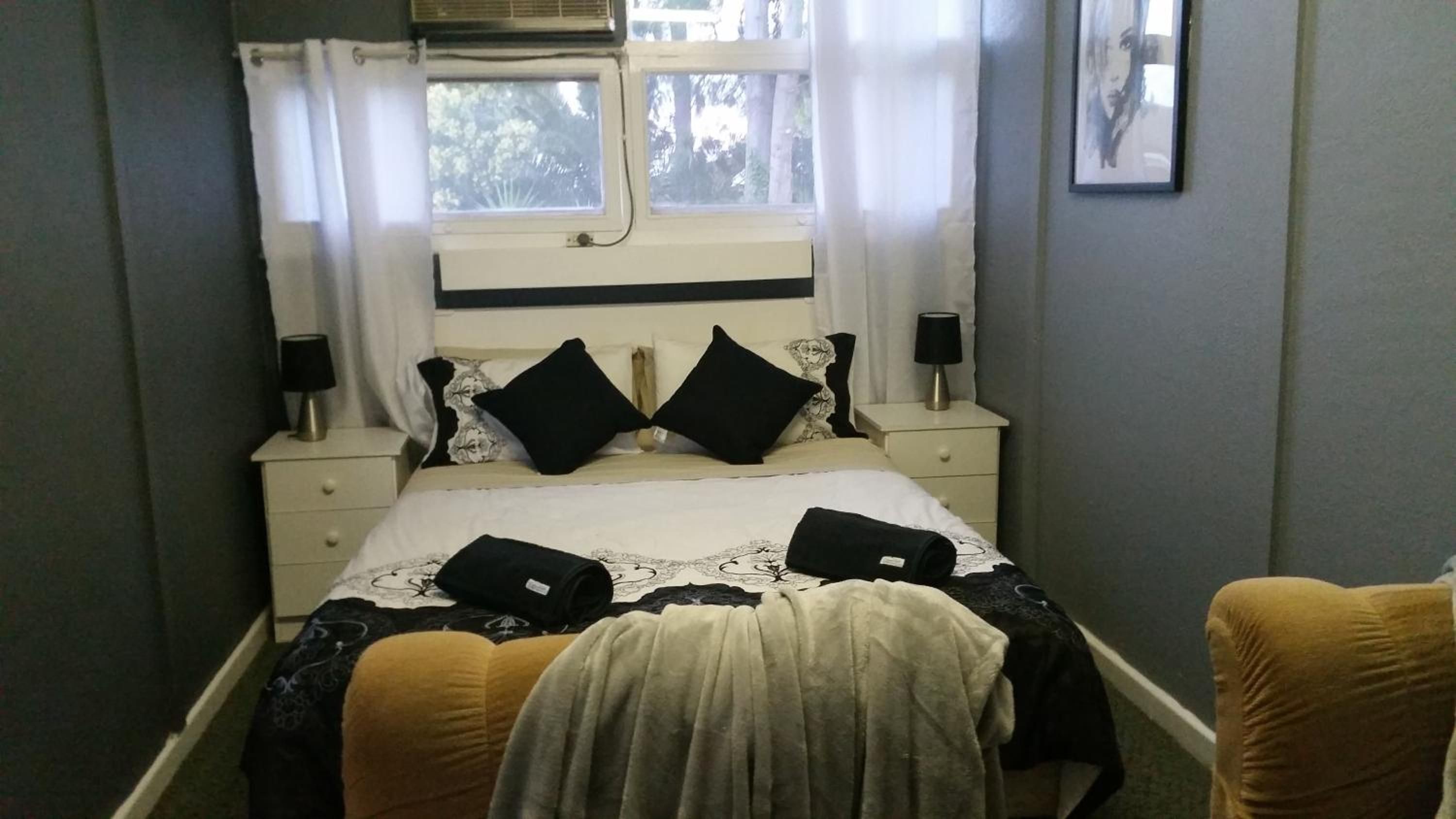 A bedroom with a bed, two bedside tables, a window with curtains, and a wall-mounted picture.