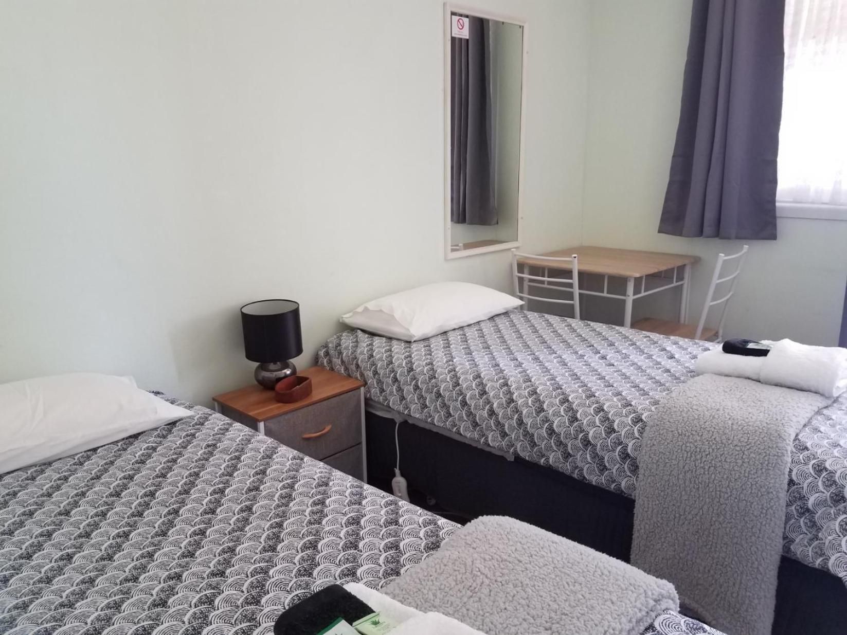 A hotel room with two beds, a desk, a chair, a lamp, and a window with curtains.