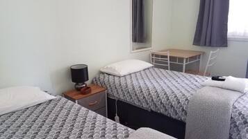 A hotel room with two beds, a desk, a chair, a lamp, and a window with curtains.