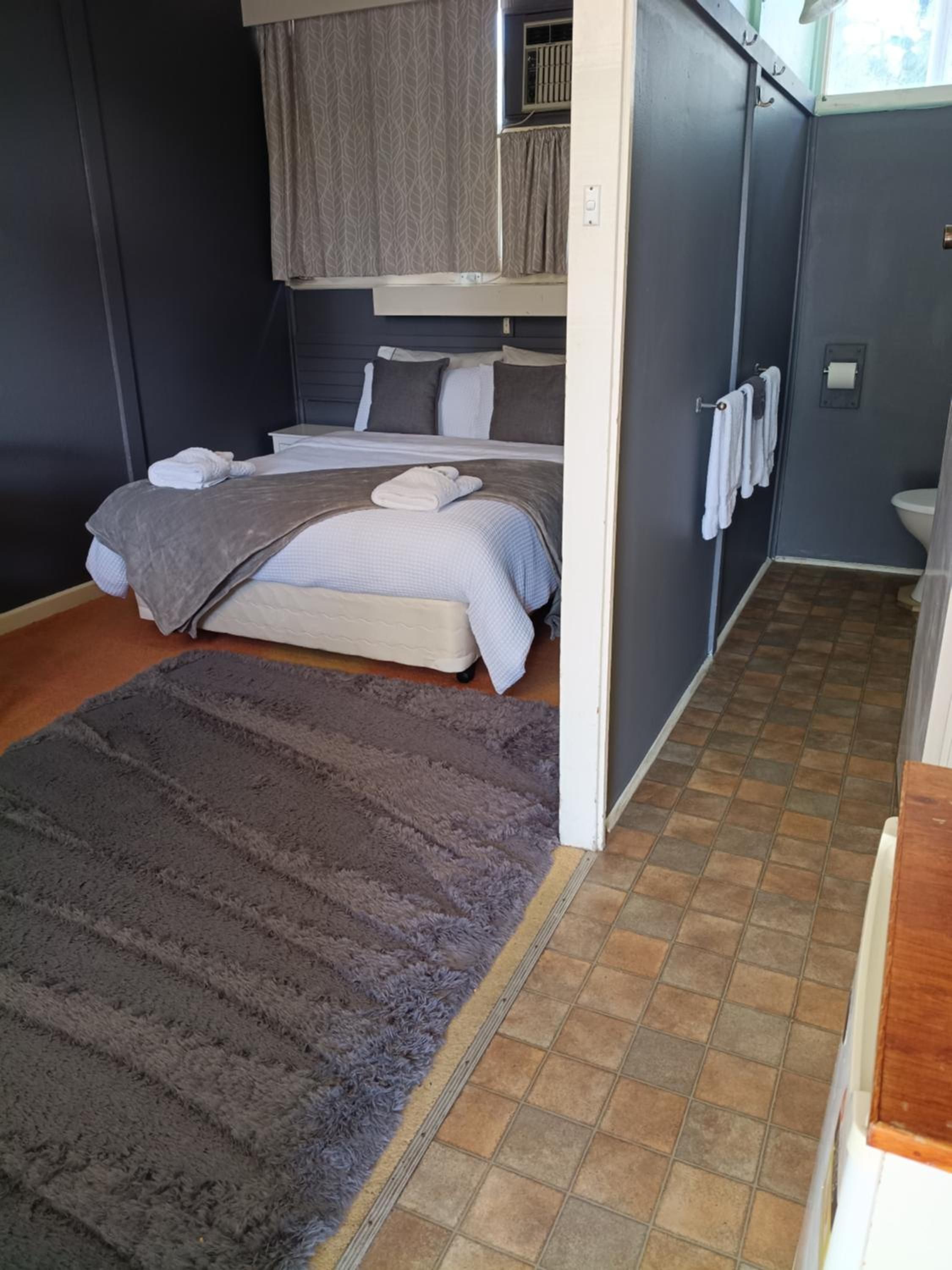 A compact room with a bed, a small bedside table, a radiator, and a view of the outside.